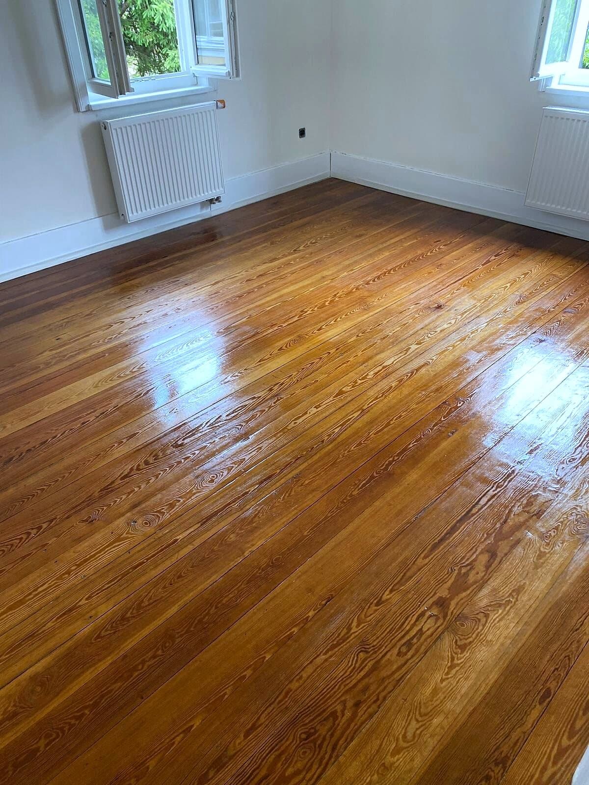 Versiegelte Holzdielen in einem hellen Zimmer mit zwei Fenstern und Heizkörpern