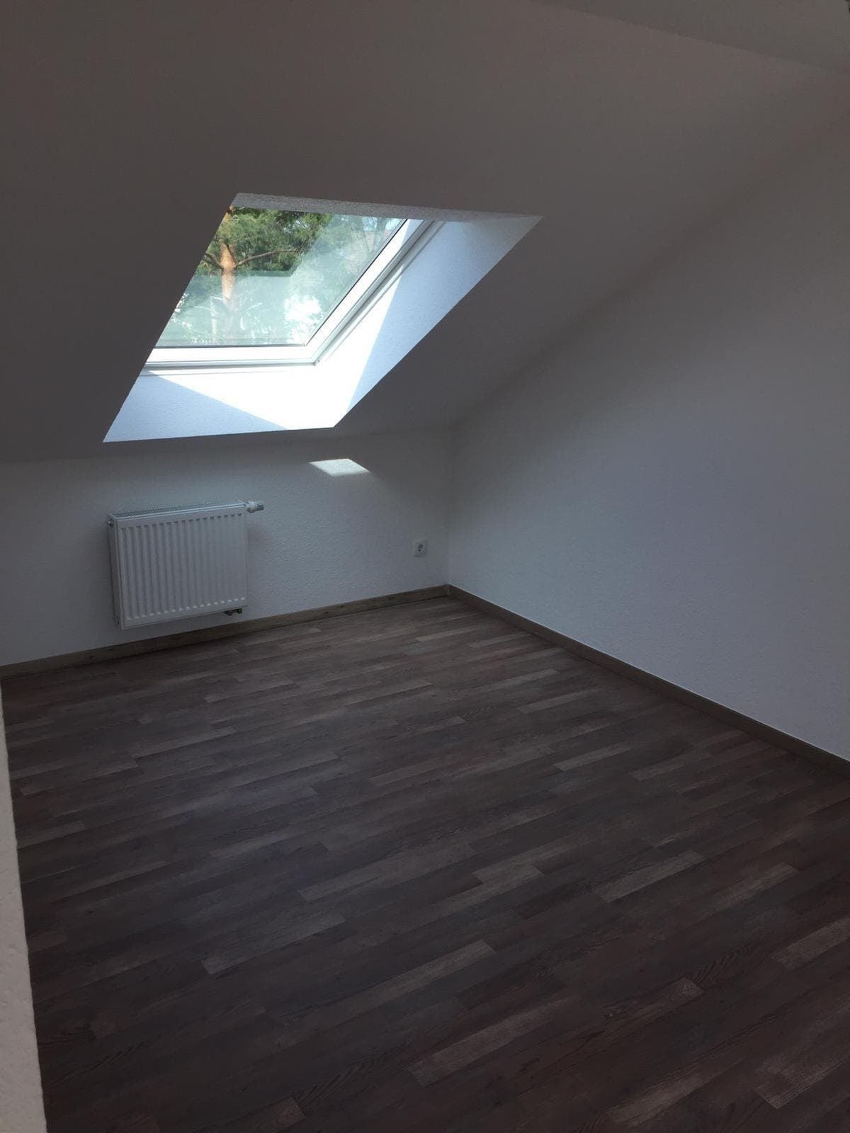 Fertig ausgebautes Dachzimmer mit Dachfenster, weißen Wänden und dunklem Boden