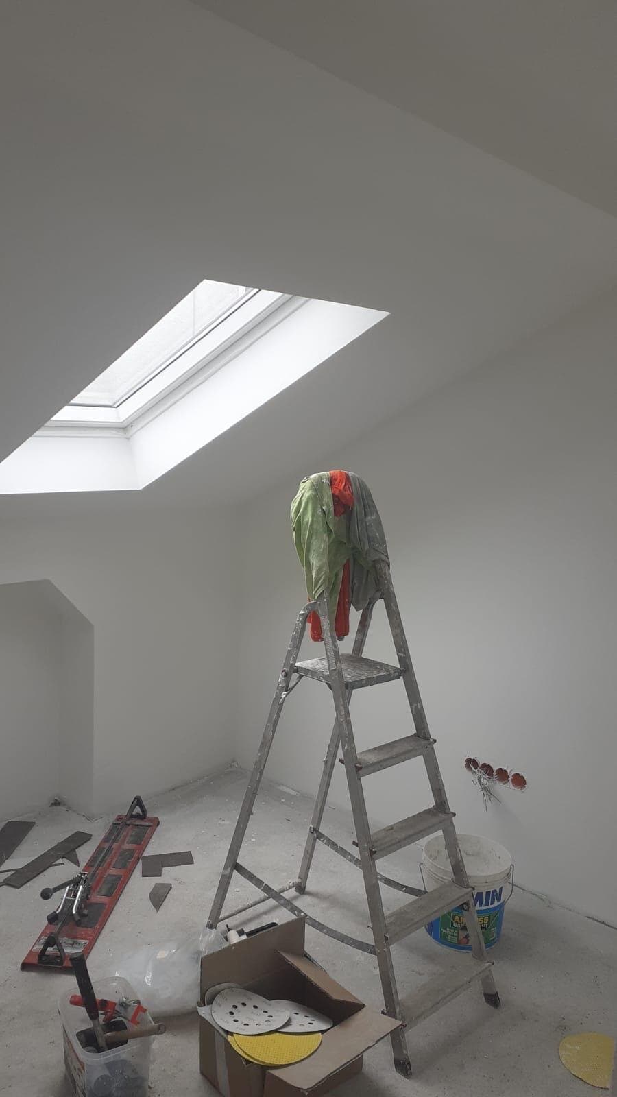 Dachgeschoss mit gespachtelten Wänden und Dachfenster, eine Leiter und Malerzubehör auf dem Boden