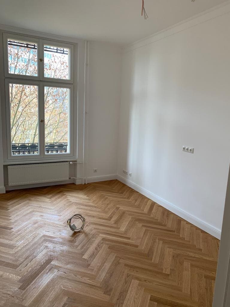Renoviertes Altbauzimmer mit Fischgrätparkett, weißen Wänden und Balkonfenster